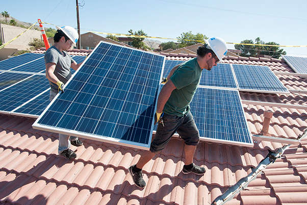 two guys carry solar panel on roof