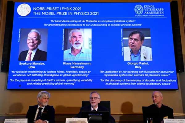 Nobel-committee-for-physics-members-sit-in-front-of-a-screen-displaying-2021-winners